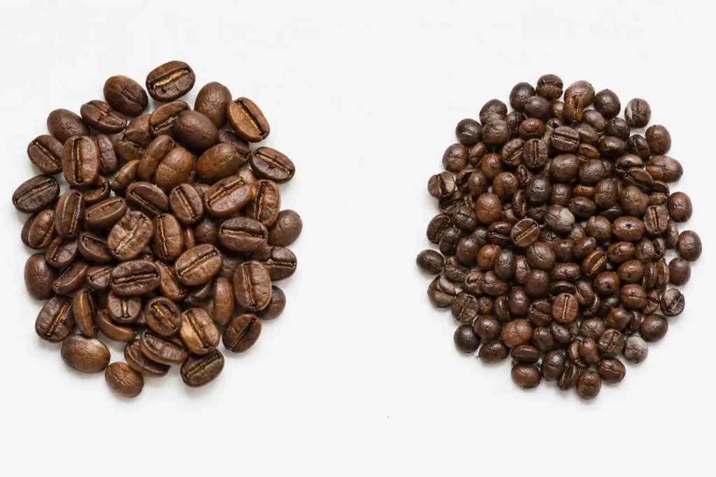 Ziarna kawy arabica i robusta wysypane obok siebie na białej powierzchni — widoczna różnica w rozmiarze i kształcie ziaren