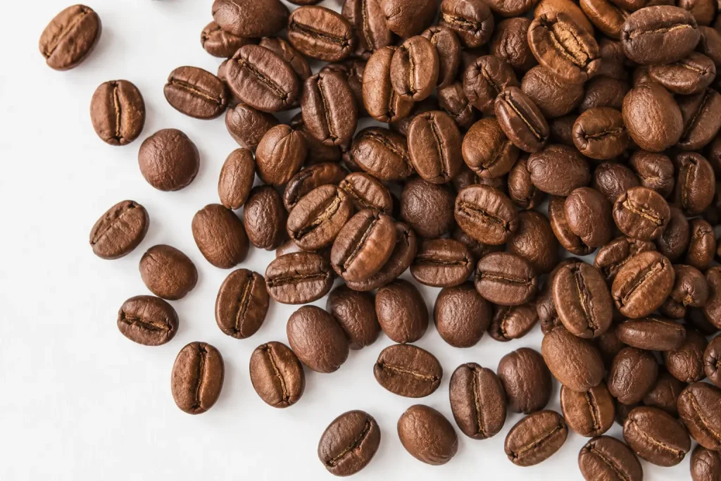 Ziarna kawy arabica wysypane na białej powierzchni — owalne, lekko spłaszczone ziarna w jasnobrązowym i ciemnobrązowym kolorze, widok z góry