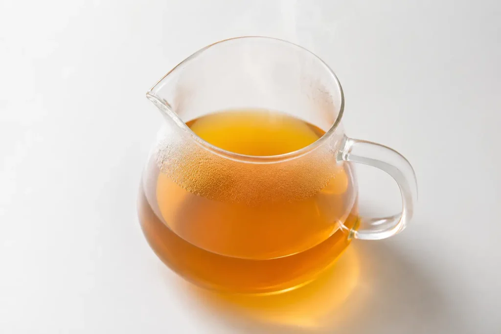 Przezroczysty szklany dzbanek z jasno zaparzoną kawą Geisha metodą pour-over — jasny złocistobrązowy napar, delikatna para unosząca się z naparu