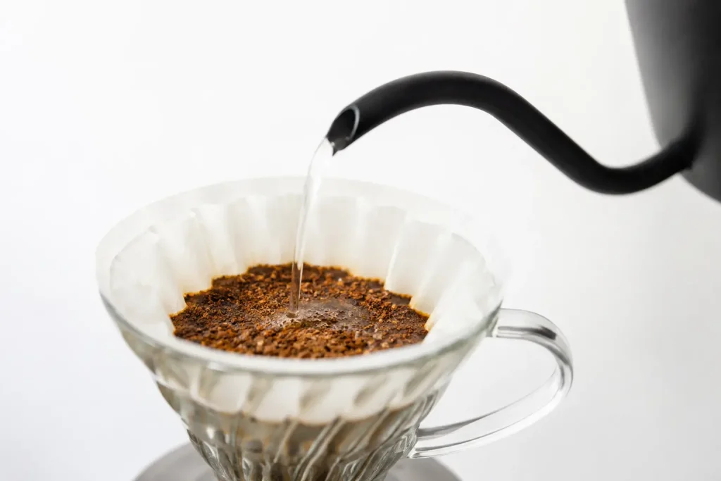 Czajnik z gęsią szyją nalewający wodę na dripper z kawą Geisha — jasne, precyzyjne parzenie metodą pour-over, białe tło, naturalne oświetlenie