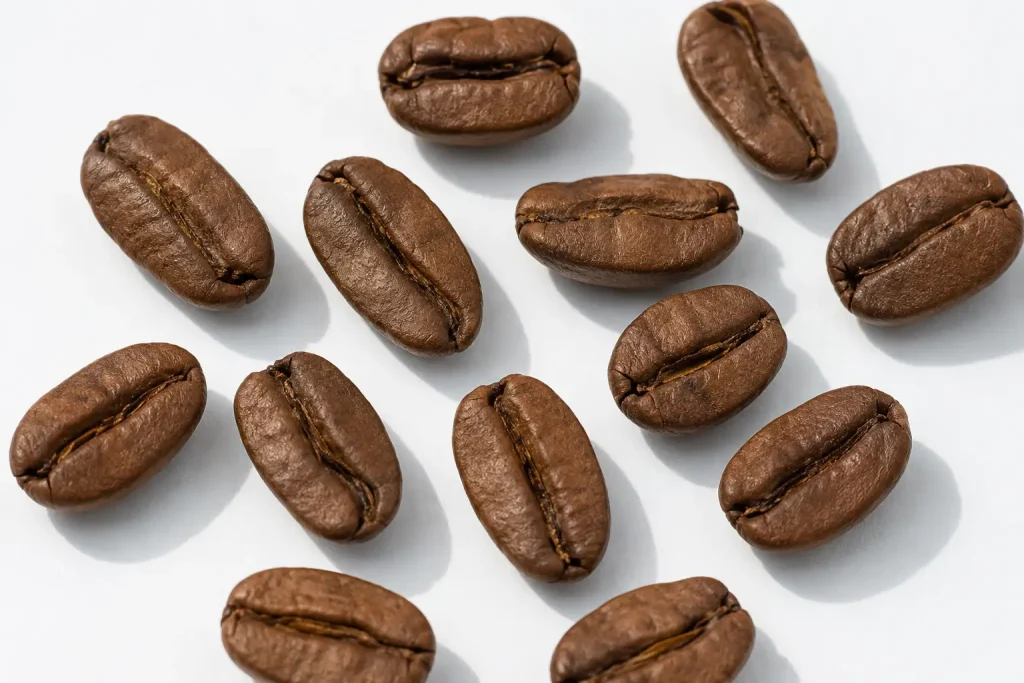 Porównanie ziaren peaberry i standardowych ziaren kawy — po lewej stronie małe, okrągłe ziarna peaberry, po prawej typowe płaskie ziarna arabiki, widok z góry na białym tle