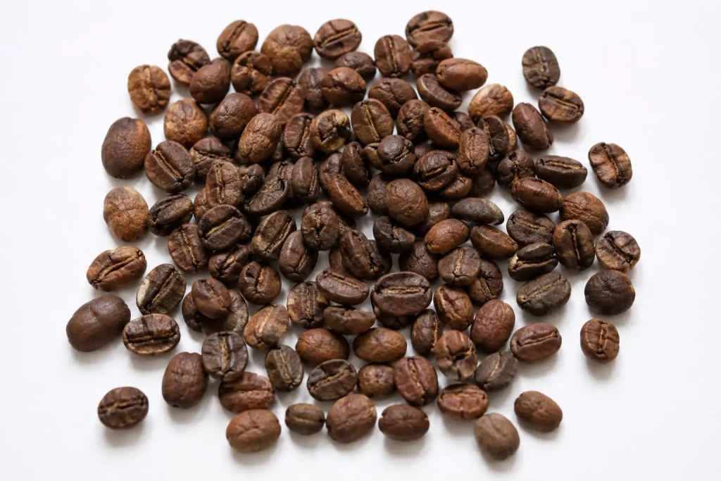  Ziarna kawy Kopi Luwak po oczyszczeniu — nieregularne, lekko jaśniejsze niż standardowe ziarna arabiki, wysypane na białej powierzchni, widok z góry