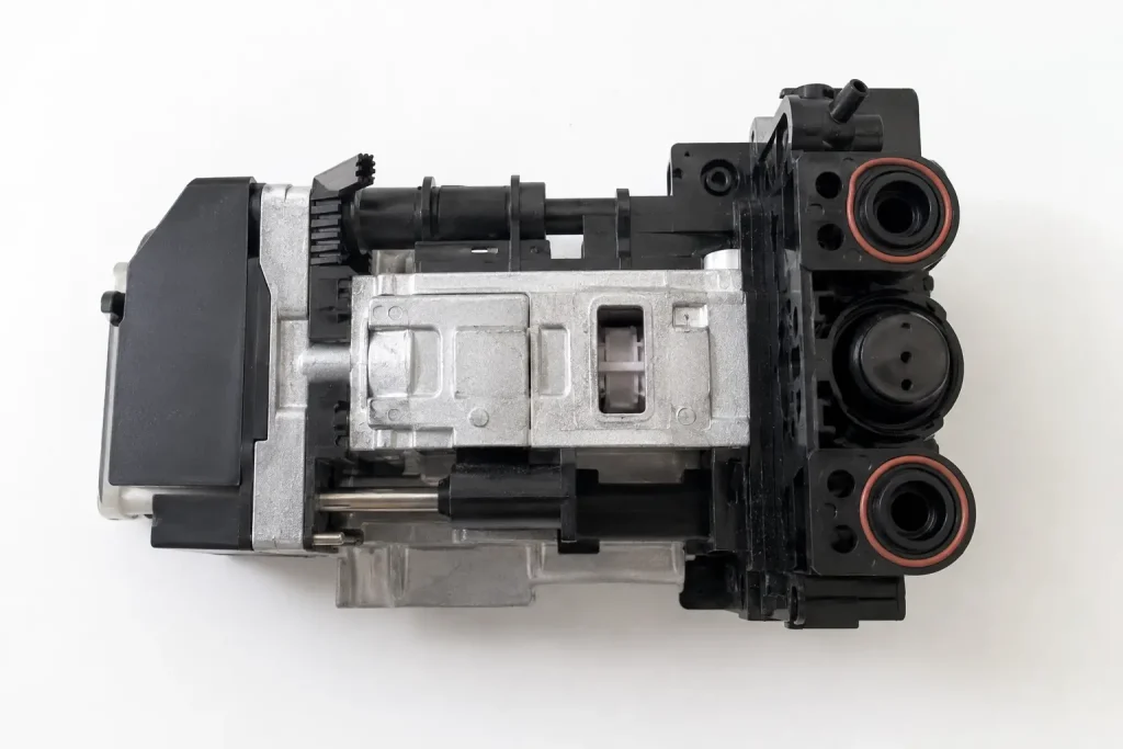 Jednostka zaparzająca ekspresu Philips Saeco wyjęta i leżąca na białej powierzchni — widoczny metalowo-plastikowy mechanizm bloku z gumowymi uszczelkami