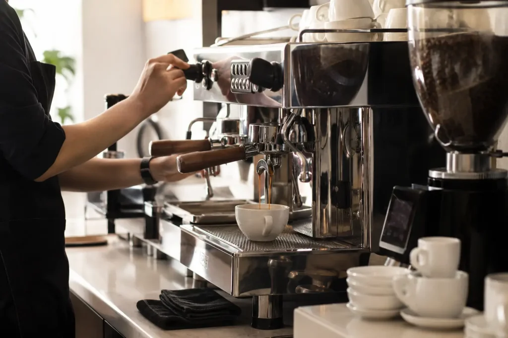 barista przy ekspresie kolbowym, młynek, portafilter i filiżanki na stanowisku pracy