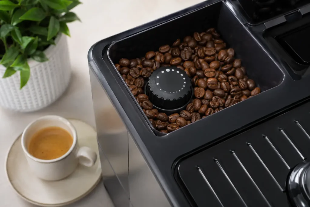  pokrętło regulacji młynka w ekspresie automatycznym, suche ziarna w zasobniku, filiżanka espresso obok bez tekstu