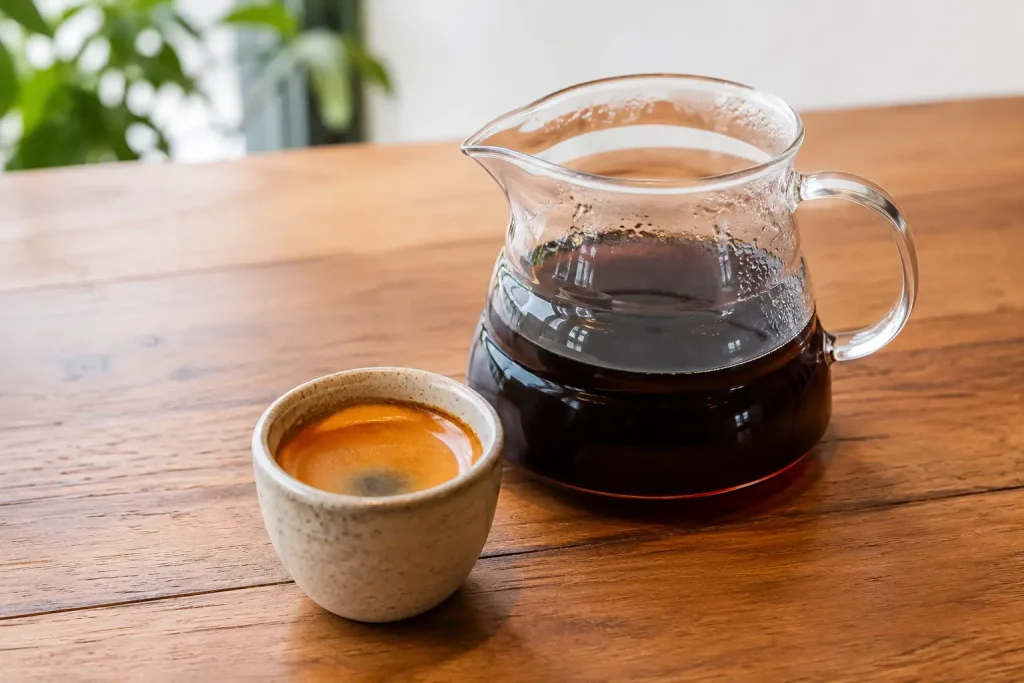 Mała filiżanka espresso z cremą oraz szklany dzbanek klarownej kawy przelewowej.