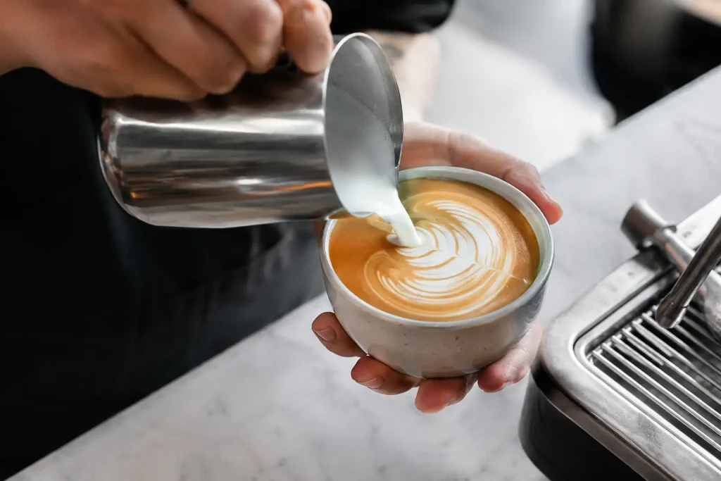 Barista przygotowujący latte art z kremowej mikropianki.
